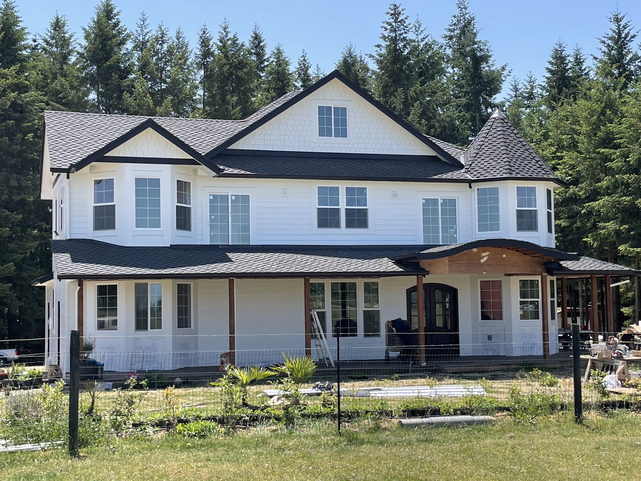 White two-story farmhouse exterior with dark trim, freshly painted, with tall firs behind