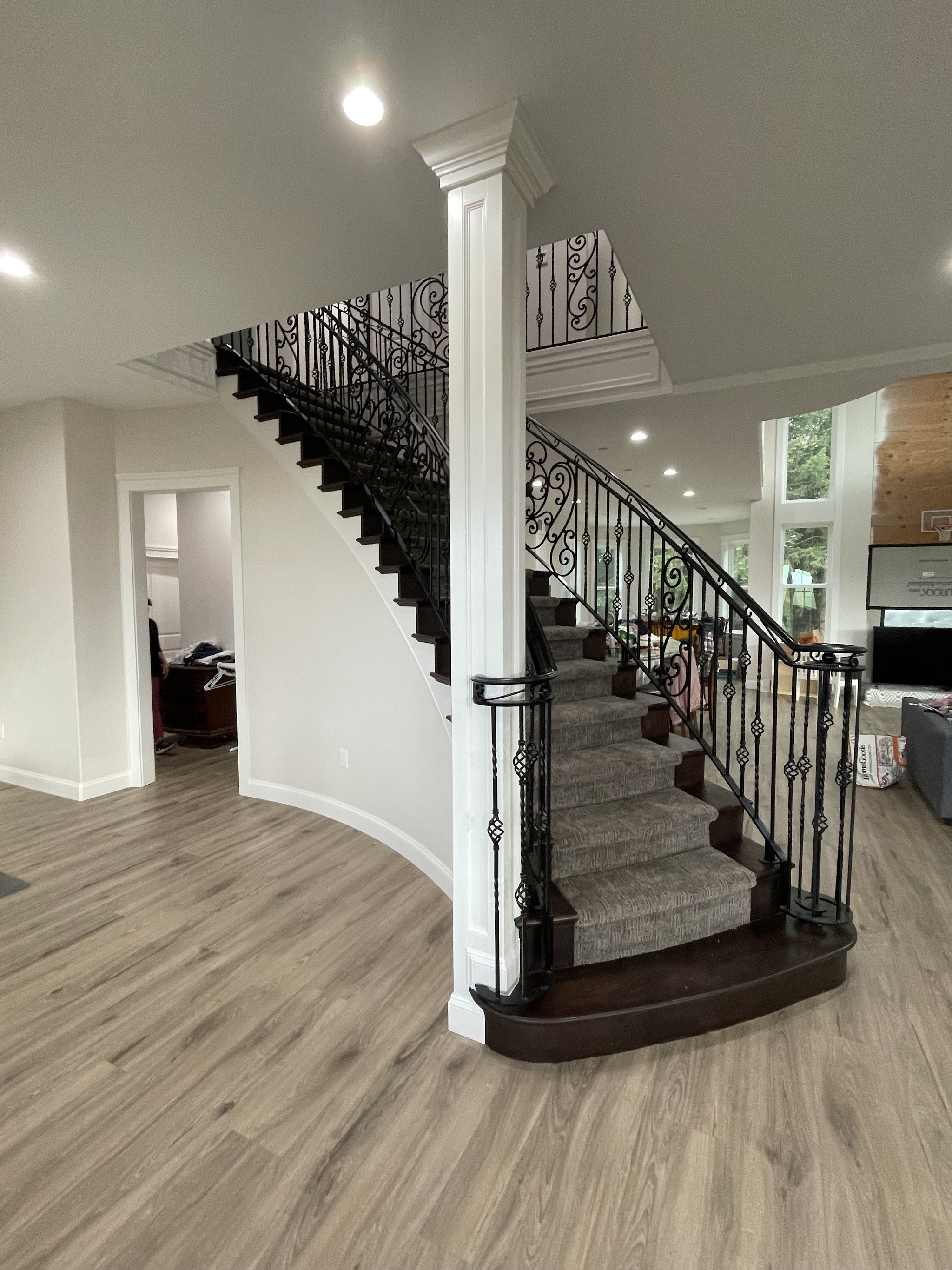 Curved staircase with wrought-iron railing, white walls and a painted column